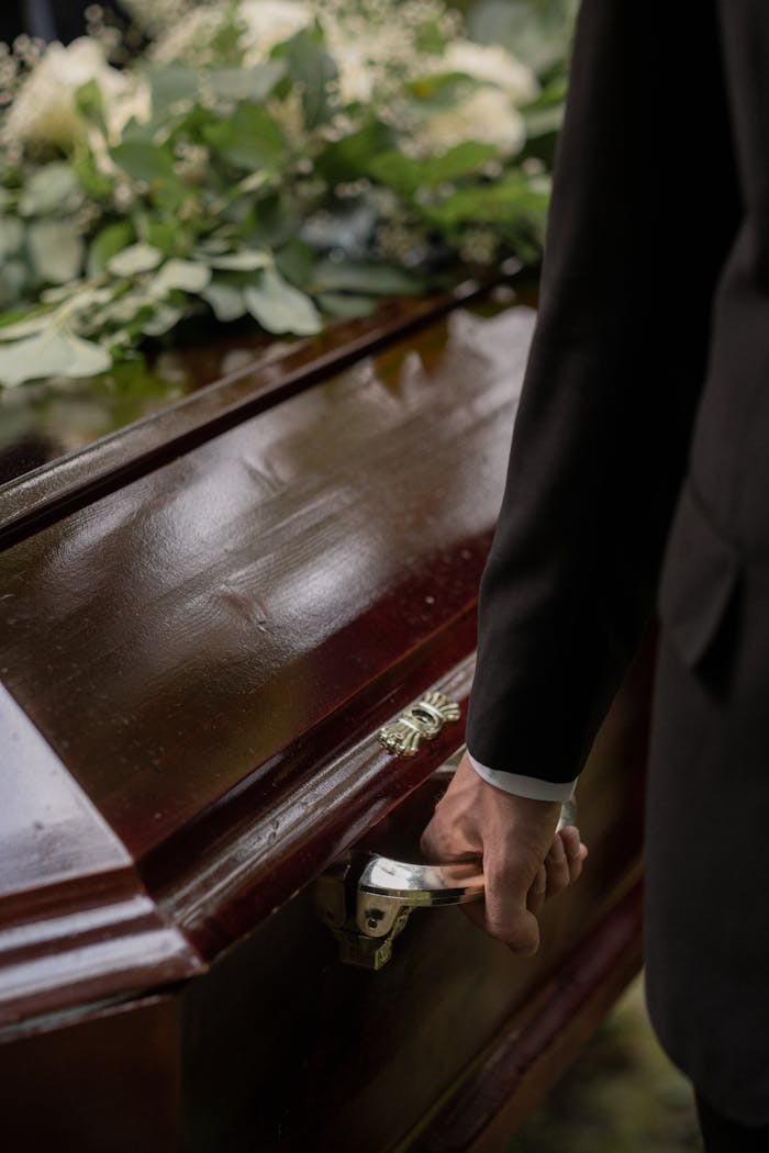 about-us Close-up of a casket with a hand holding the handle during a funeral.