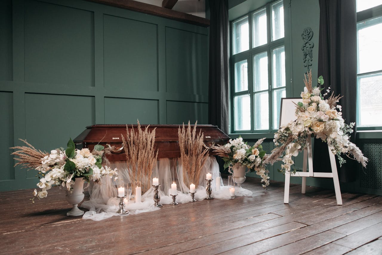 our-story An indoor funeral setting with a wooden coffin, white flowers, and lit candles.